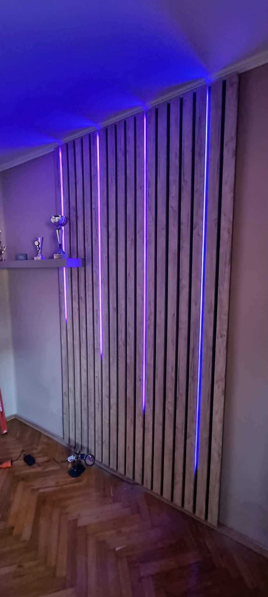 Ferde mennyezetig futó lamellás fafal kék-lila LED szalagokkal a nappaliban